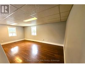 A room with wooden flooring and two windows.