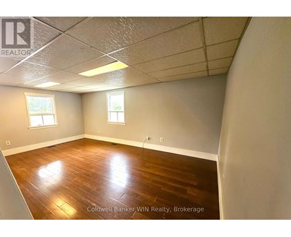 A room with wooden flooring and two windows.