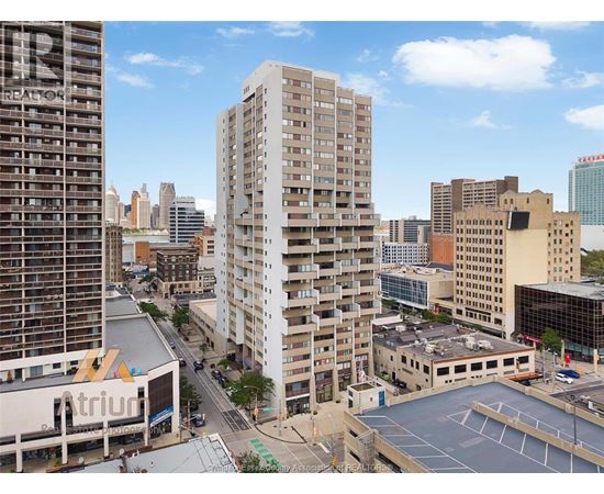 A cityscape with a tall building in the foreground and a parking lot in the middle ground.