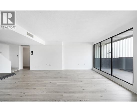 A spacious room with wooden flooring and white walls, featuring a glass door and a staircase.