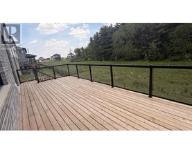 A wooden deck with a black railing overlooks a grassy area.
