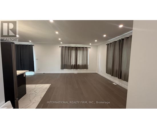 A spacious room with wooden flooring and a large window with curtains.