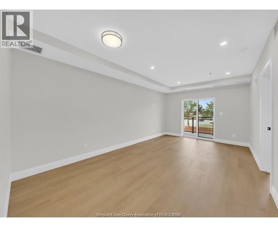 A spacious room with wooden flooring and a sliding glass door leading to a balcony.