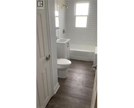A white toilet is in a bathroom with a white tub and a window.