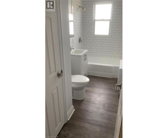 A white toilet is in a bathroom with a white tub and a window.