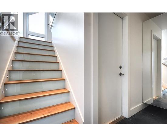 A set of stairs with a glass balustrade and wooden steps leading to a white door.