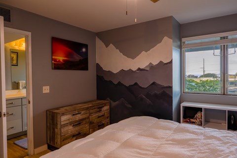 A bedroom with a bed, a wooden dresser, and a wall mural.