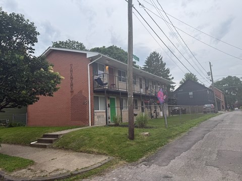 A red brick building with a green door sits on a street with a sidewalk.