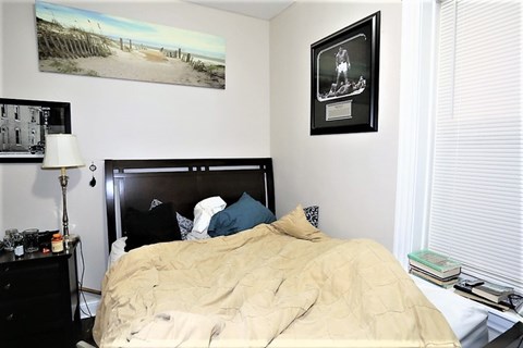 A bedroom with a bed, a nightstand with a lamp, and a picture on the wall.