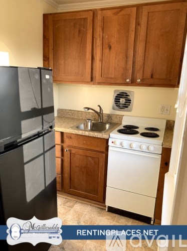 A kitchen with a black fridge, white stove and wooden cabinets.