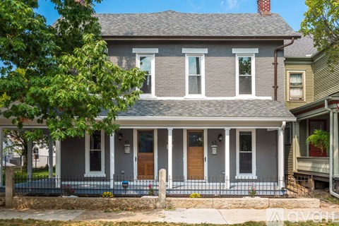 A grey house with a brown door and a black fence.