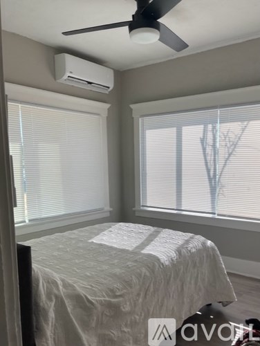A bedroom with a bed, a ceiling fan, and a window with blinds.