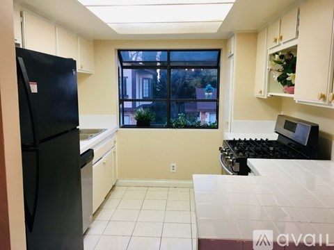 A kitchen with a black fridge, white countertops, and a window overlooking a house.