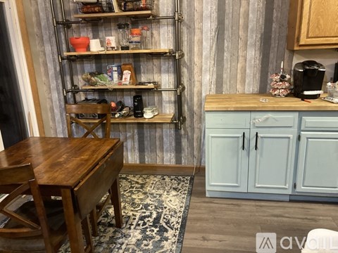 A kitchen with a wooden table and chairs, a shelf with various items, and a cabinet with a coffee maker.