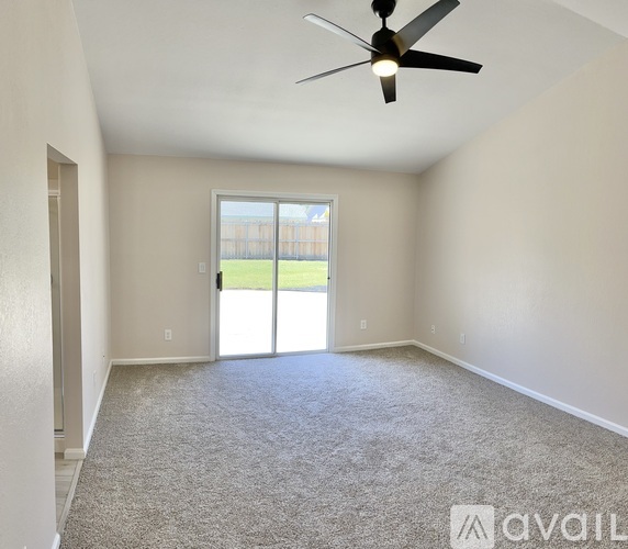 A spacious room with a ceiling fan and sliding glass doors leading to a backyard.
