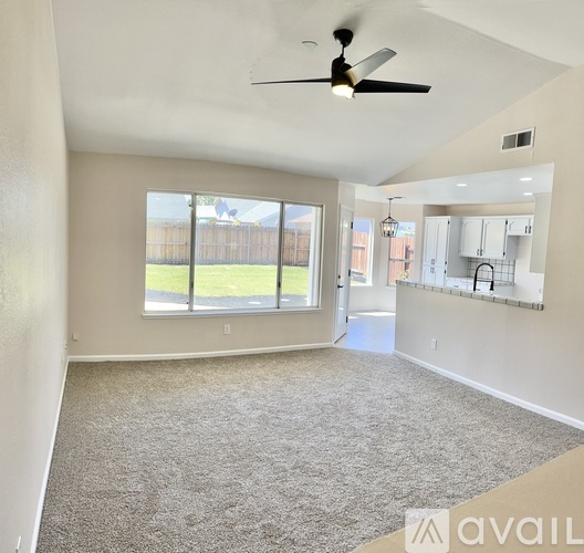 A spacious living room with a ceiling fan and a view of a backyard through a large window.