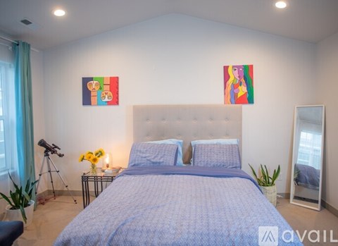 A bedroom with a large bed and two colorful paintings on the wall.