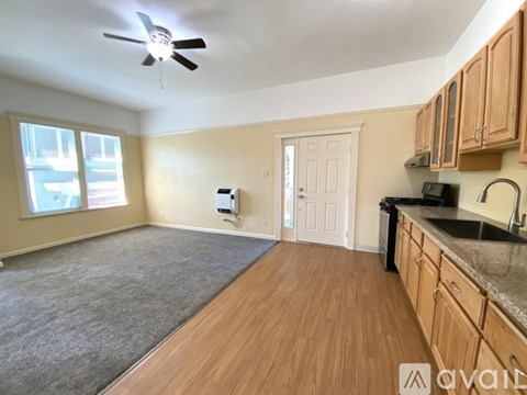 A room with wooden floors and a kitchen area with a sink and stove.