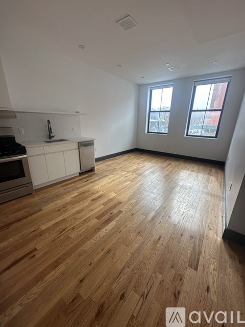 A spacious room with wooden flooring and a kitchen area with white cabinets and a stove.