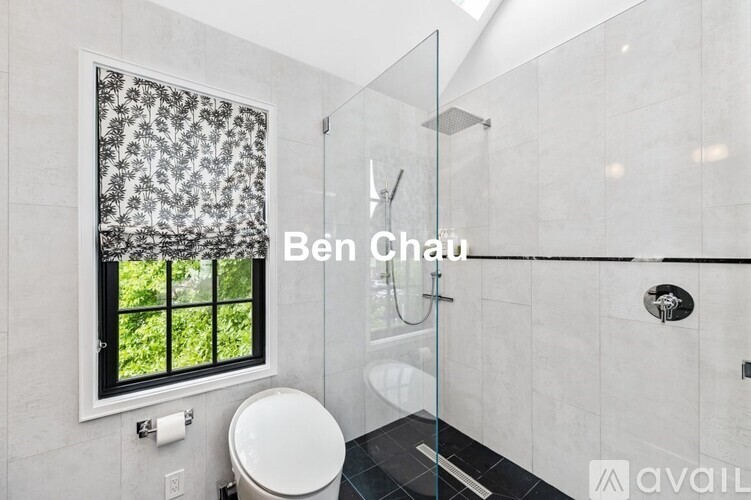 A bathroom with a toilet, a window with a view of trees, and a glass shower stall.