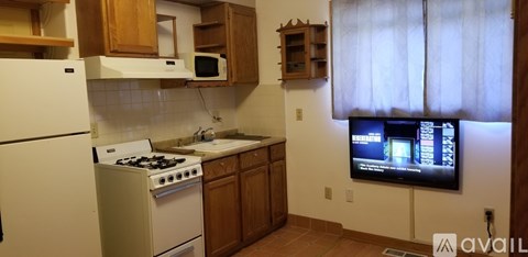 A small kitchen with a white refrigerator and a TV mounted on the wall.