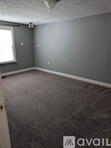 A room with grey walls and carpeting is available for rent.