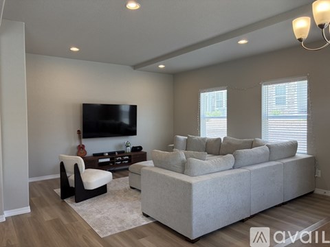 A living room with a grey sofa, a black chair, and a television on the wall.