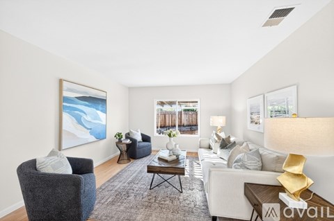 A living room with a grey armchair, a white sofa, a coffee table, and a painting on the wall.