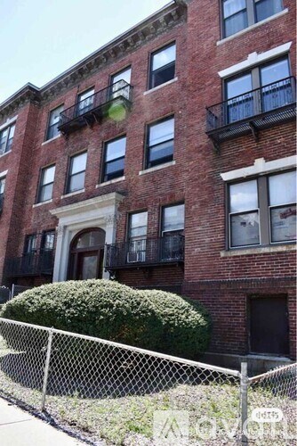 A red brick building with a black fence and a bushy green bush.