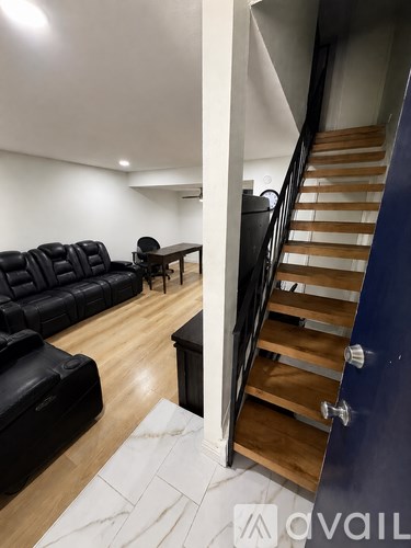 A black leather sofa sits in a spacious living room with a wooden staircase.