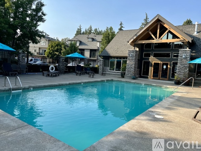 A large outdoor swimming pool with a stone border and a wooden deck house in the background.