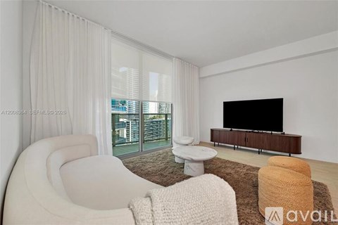 A living room with a white chair, a brown rug, and a black television.