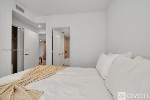 A bedroom with a bed covered in a white sheet and a tan blanket.