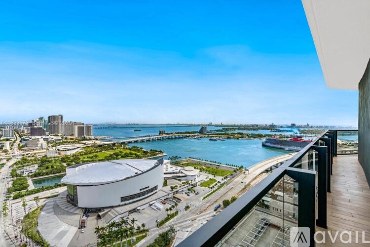 A modern building with a curved roof is situated on a balcony overlooking a waterfront with boats and a city skyline.