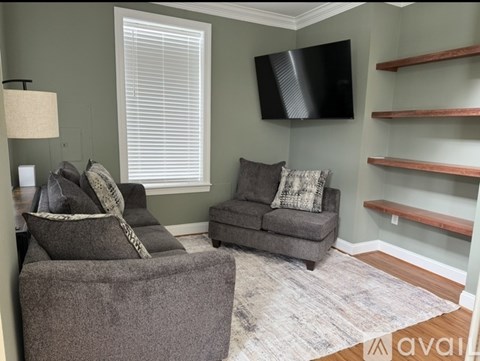 A living room with a grey couch, a grey ottoman, a flat screen TV and a rug.