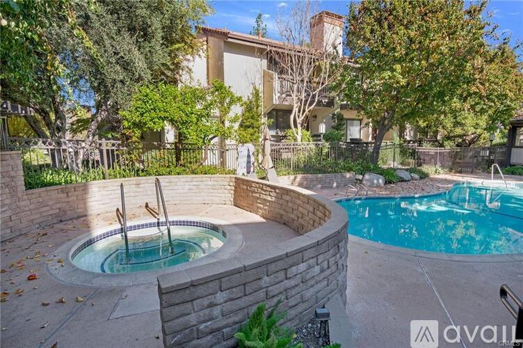 A hot tub sits in the middle of a backyard with a pool and a house in the background.