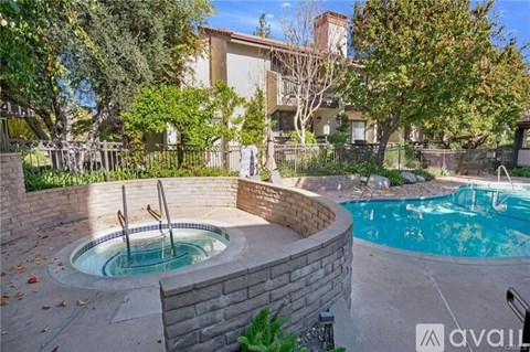 A hot tub sits in the middle of a backyard with a pool and a house in the background.