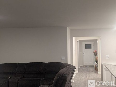 A black couch sits in a living room with a doorway leading to another room.
