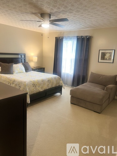 A bedroom with a bed, chair, and a ceiling fan.