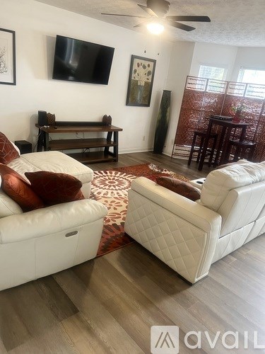 A living room with two white couches and a television mounted on the wall.
