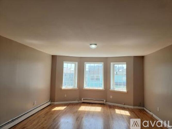A spacious room with wooden floors and three windows.