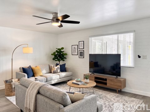A living room with a grey couch, a coffee table, a television, and a ceiling fan.