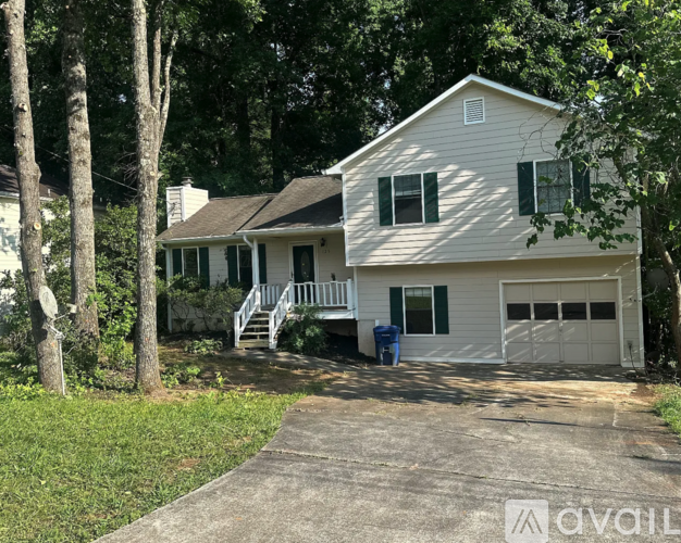 A house with a garage and a driveway is surrounded by trees.