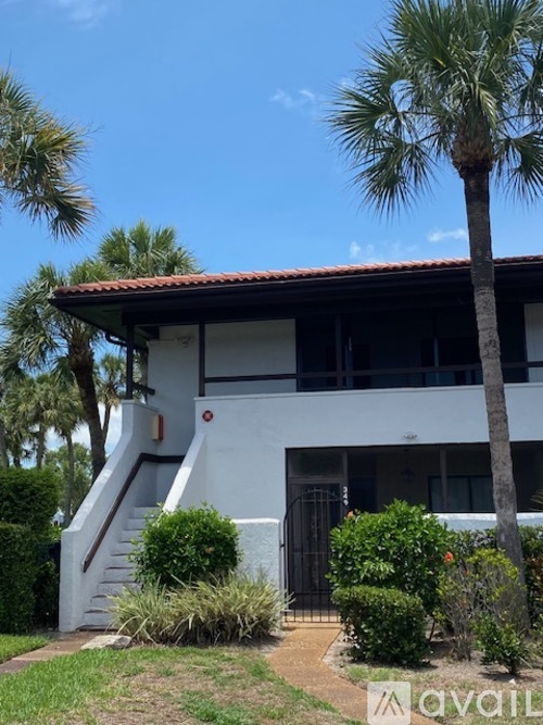 A white house with a red tile roof and a palm tree in front.