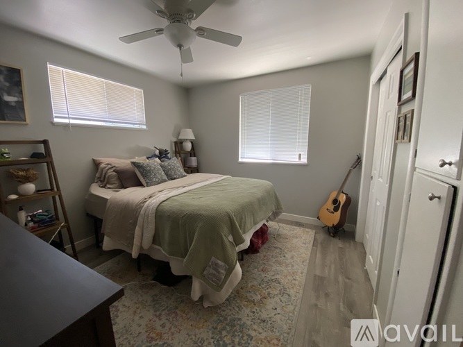 A bedroom with a bed, a guitar, and a ceiling fan.