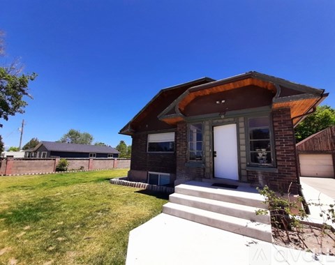 A house with a brown roof and a white door is surrounded by a grassy lawn.