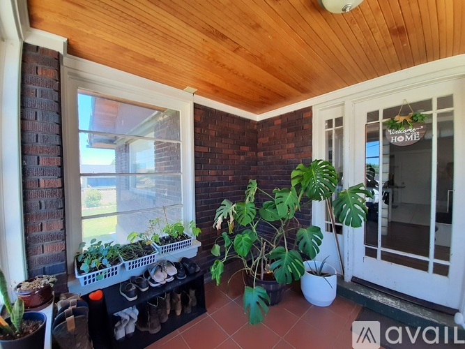 A balcony with a wooden ceiling, a brick wall, and a variety of potted plants.