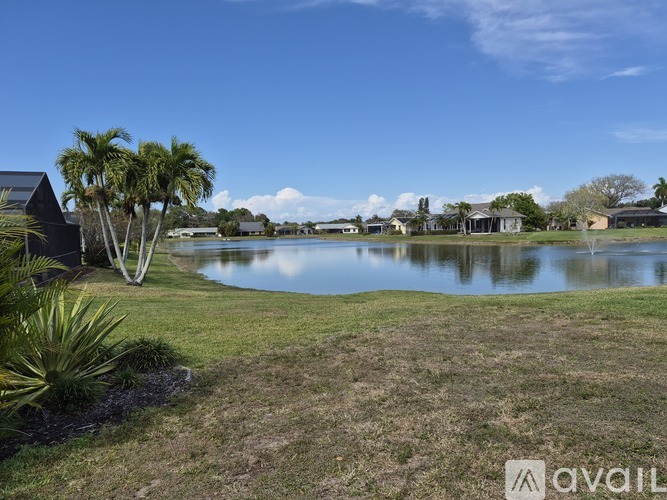 A serene landscape with a pond, palm trees, and a clear sky.