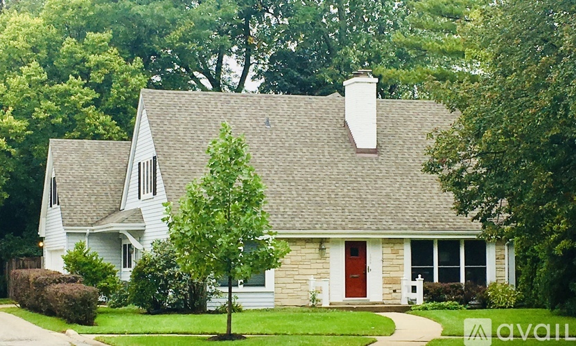 A house with a red door and a chimney is surrounded by greenery.