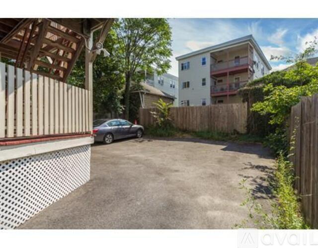 A car is parked in a driveway next to a white building with a wooden fence.